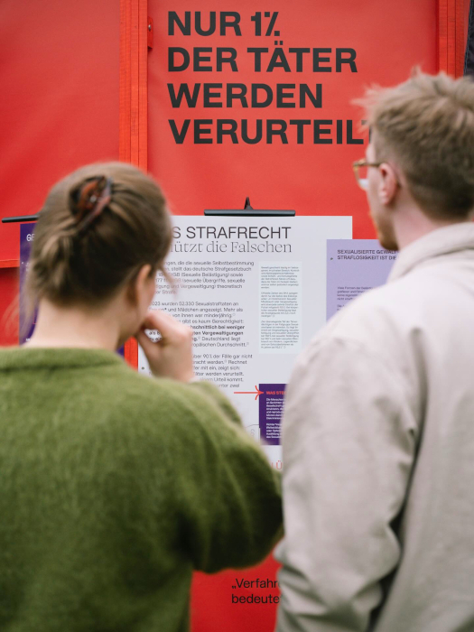 Zwei Personen betrachten einen Teil der Installation „Gewalten Formen“ mit dem Text „Nur 1% der Täter werden verurteilt“