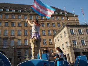 eine Person schwenkt eine Trans-Flagge vor dem Bochumer Rathaus