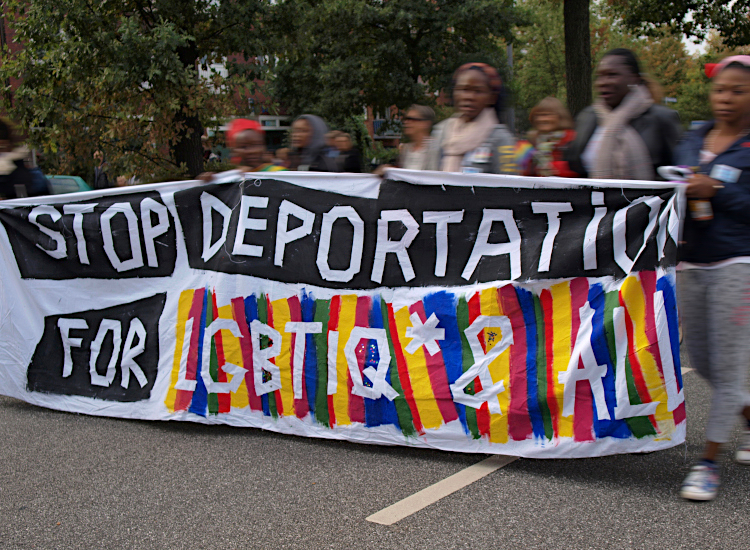 Mehrere Schwarze Frauen* tragen ein Transparent mit der Aufschrift: „Stop deportation for LGBTIQ* & all“