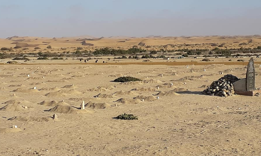 Gedenktafel für die während der deutschen Kolonialzeit in Konzentrationslagern ermordeten Ovaherero und Nama vor einer Sandfläche mit namenlosen Gräbdern in Swakopmund, Namibia